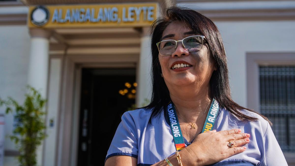 Nurse Karen Dames is standing in front of the Alangalang, Leyte Rural Health Unit with her hand on her heart.