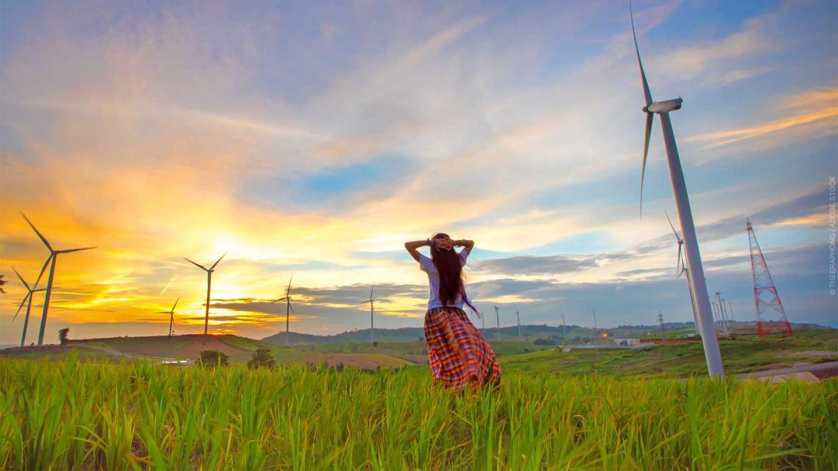 Happy woman relaxing with wind generators turbines beautiful sunset background.
