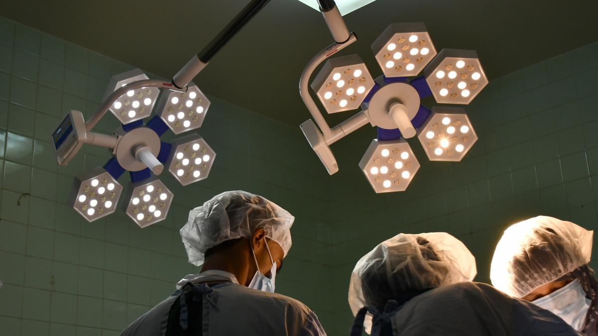 Overhead lights shine down on doctors and nurses working in a hospital. 