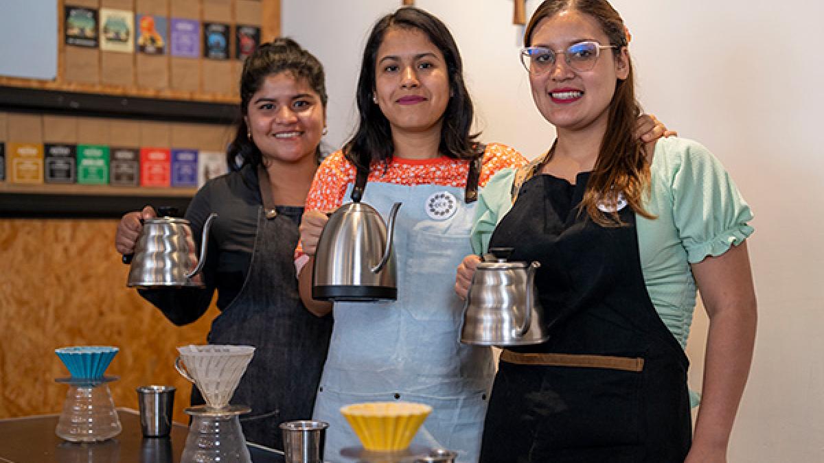 Three young barista women smiling and holding pots of brewed coffee