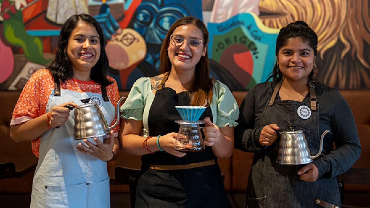 Tres mujeres jóvenes sonriendo y sosteniendo jarras de café filtrado