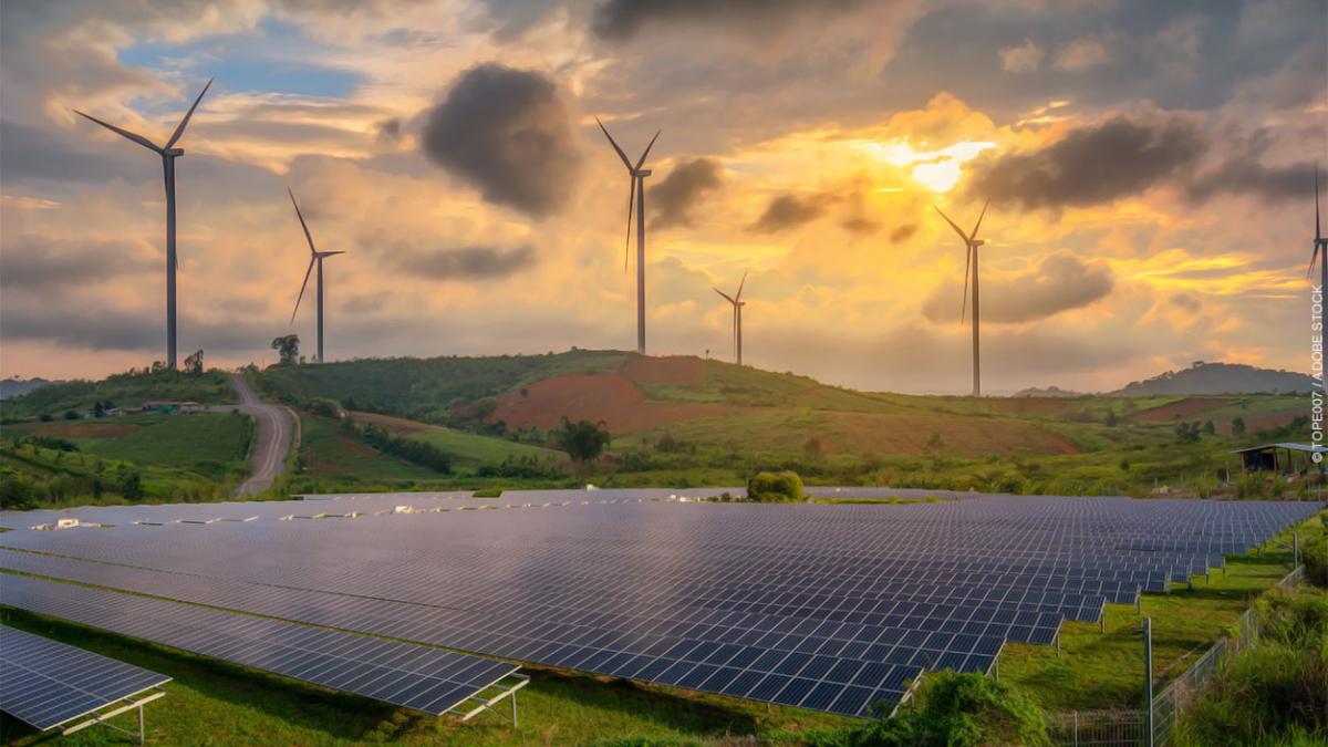 A photo of windmills and solar panels in a field at sunset