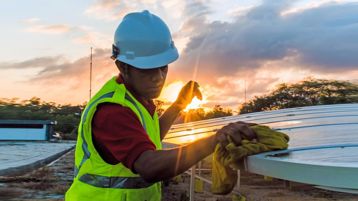 A solar technician cleans photovoltaic panels while the sun sets in the background