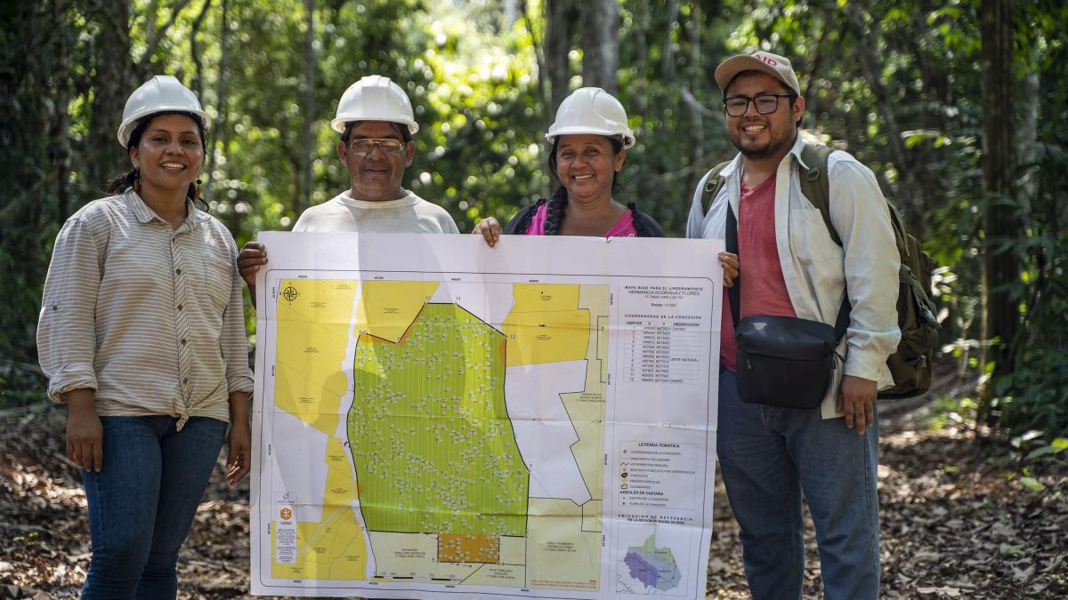 Four people holding and showing off a map of a forest concession on the Amazon rainforest