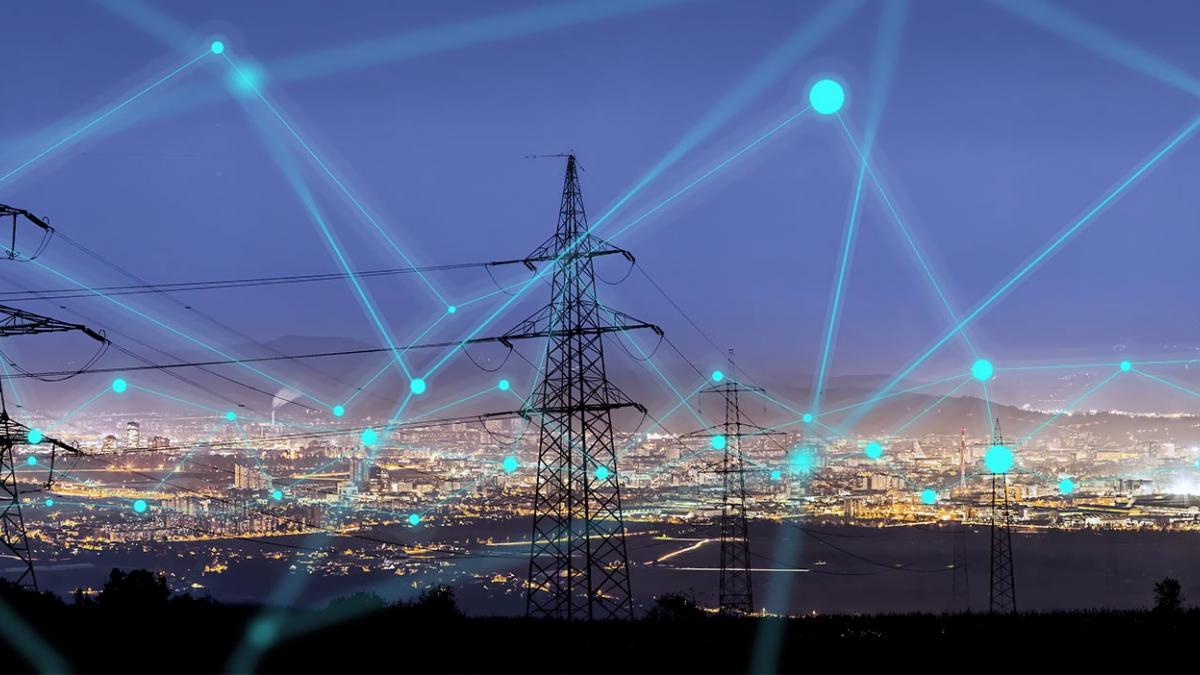 A cityscape at night with high power energy transmission towers in the foreground. A network of lines and dots of light are superimposed over the image to evoke the concept of the smart energy grid.