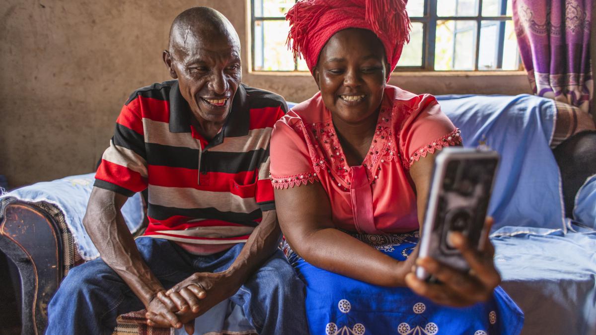 A mom and dad smile while talking to their son over a smartphone.