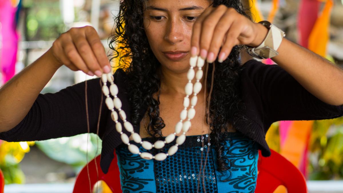 A woman holds a white necklace.
