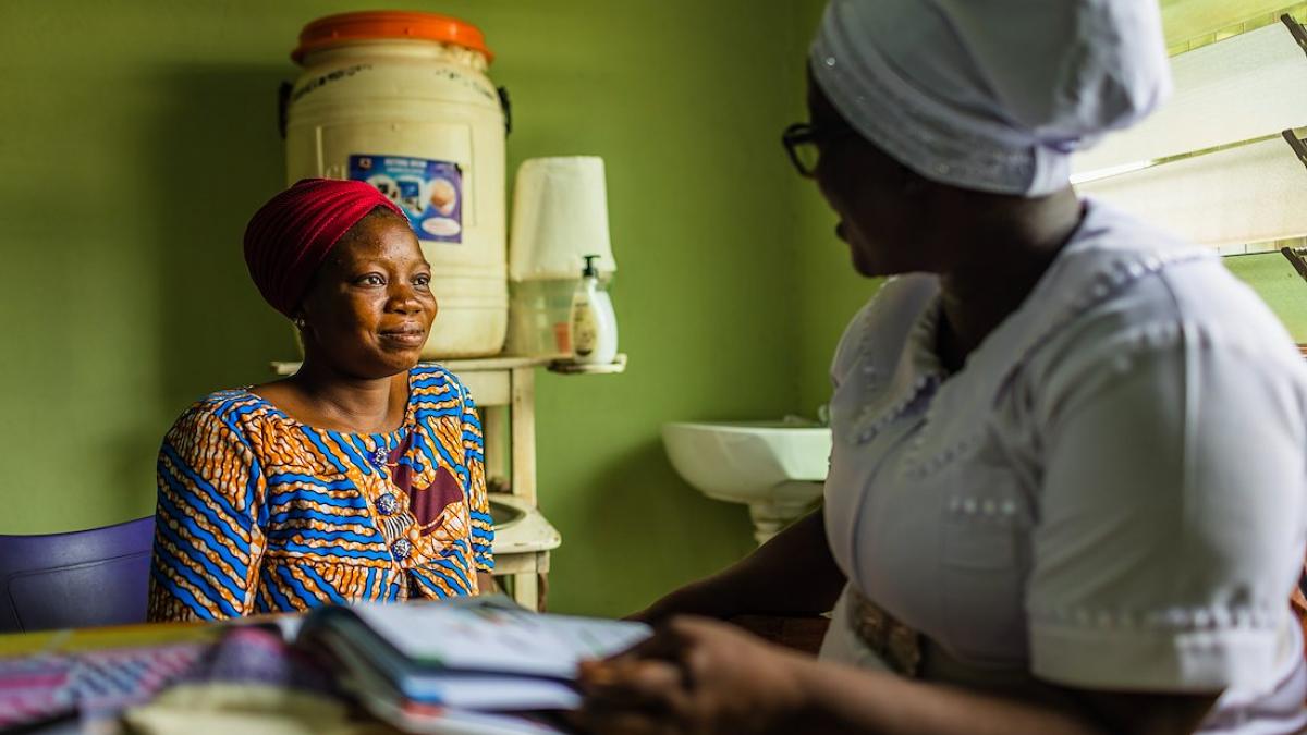 Adama speaks with a female patient in her office where she conducts checkups, writes care plans, monitors and administers medication, such as antimalarials, and offers parents and caregivers advice on the care of newborns.
