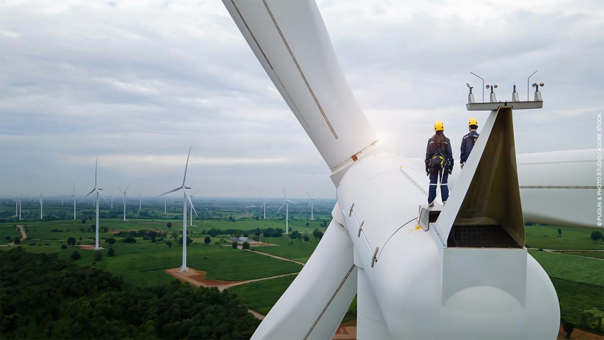 Two electricians stand on top of a wind turbine.