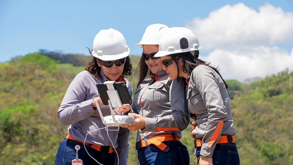 Three female Celsia technicians in safety gear operate a drone to inspect power equipment.