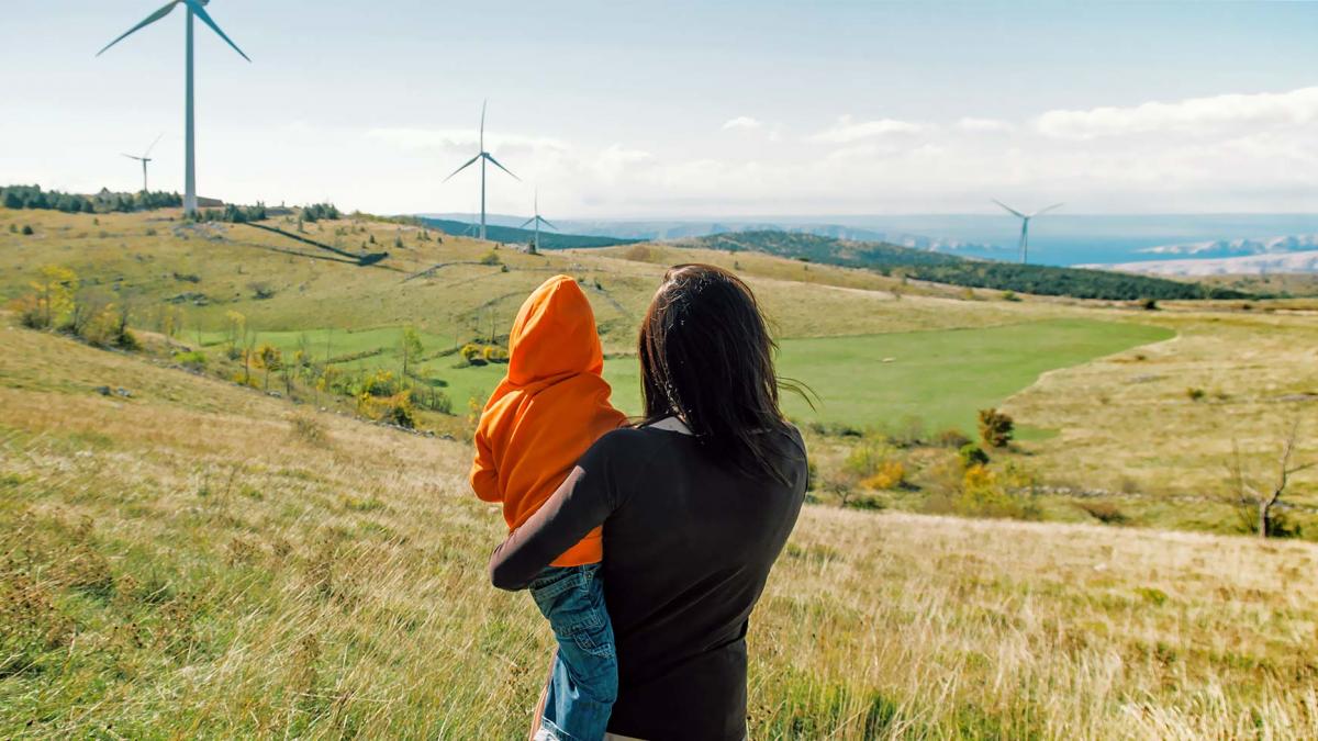 Mother holding her son in nature. Wind turbines in the background.