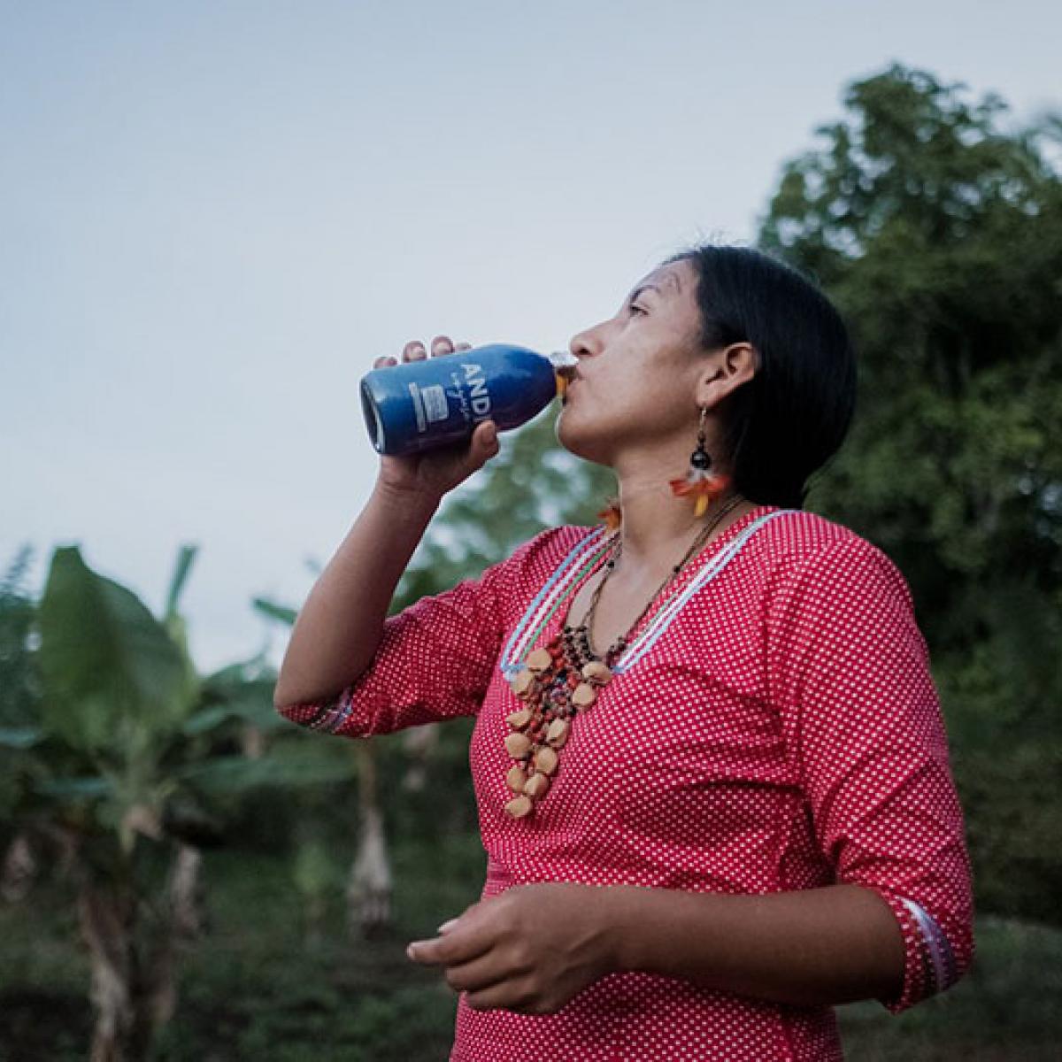 An indigenous woman drinking from a bottle of an Amazonian energizing beverage