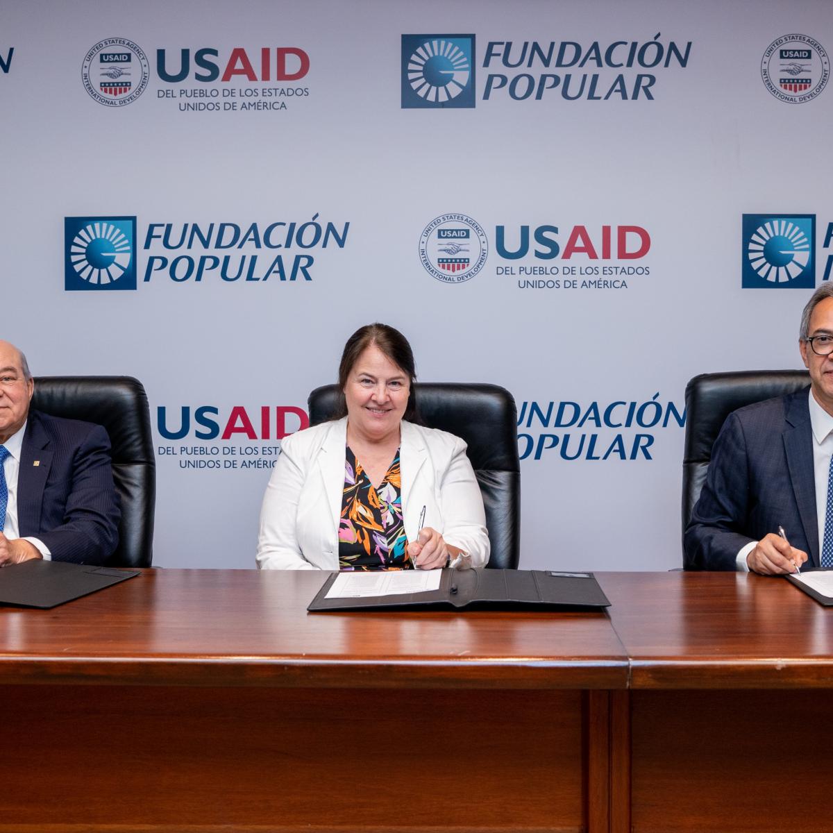 Two Banco Popular executives sign a MOU with the USAID/DR Mission Director.