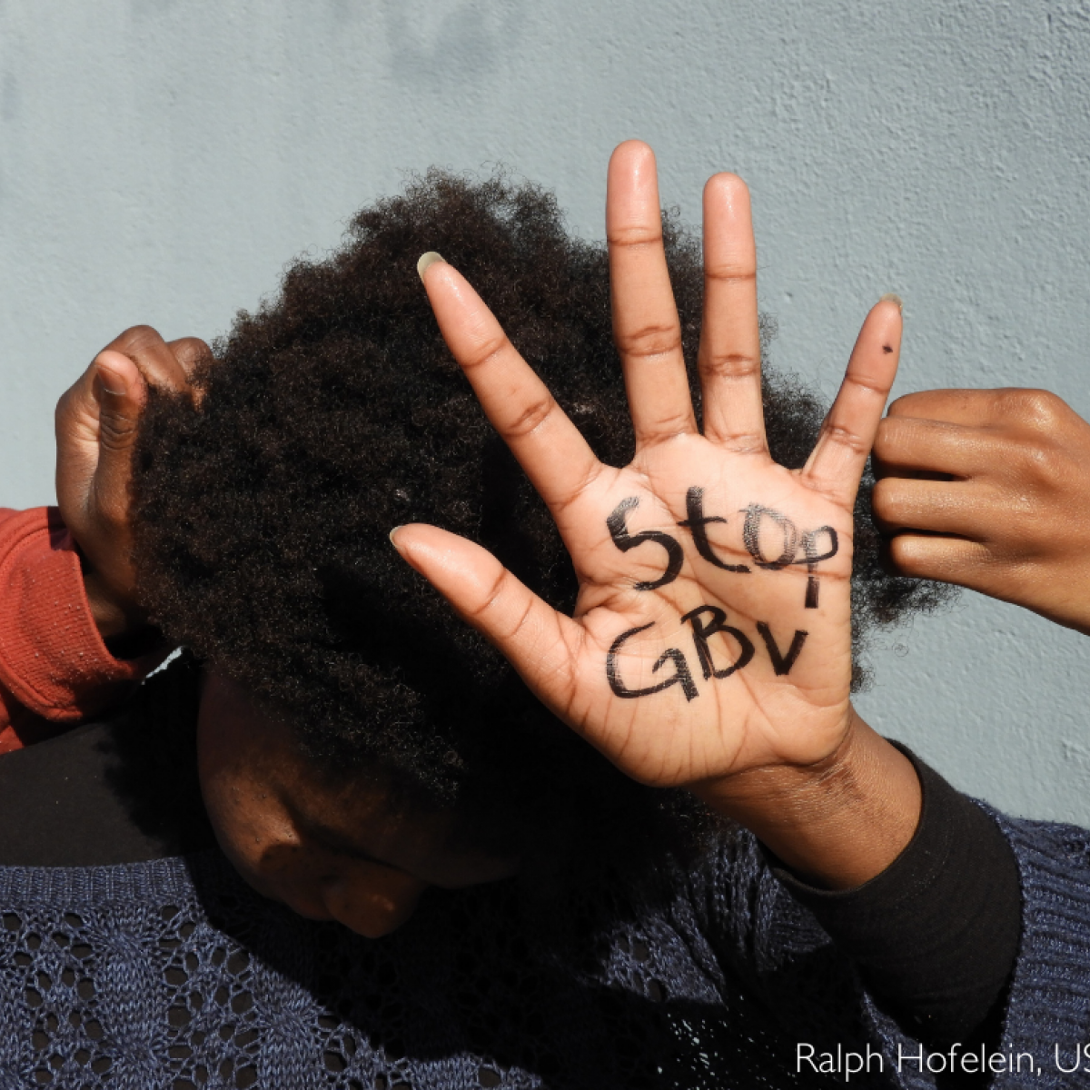 A woman shows her hand with the words "Stop GBV"