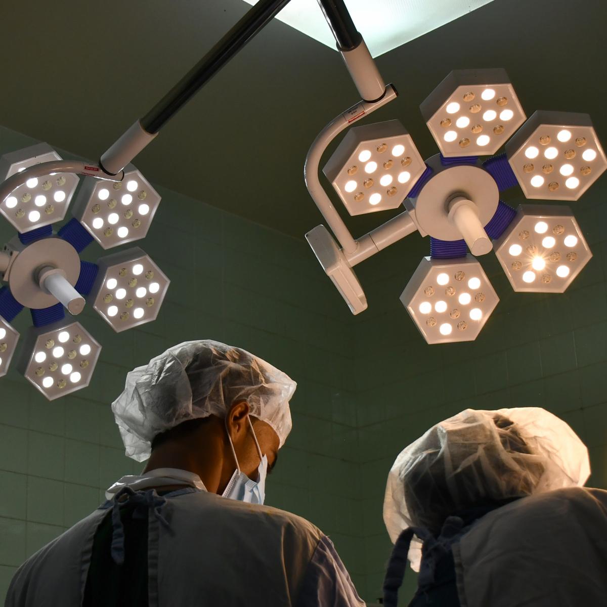 Overhead lights shine down on doctors and nurses working in a hospital. 