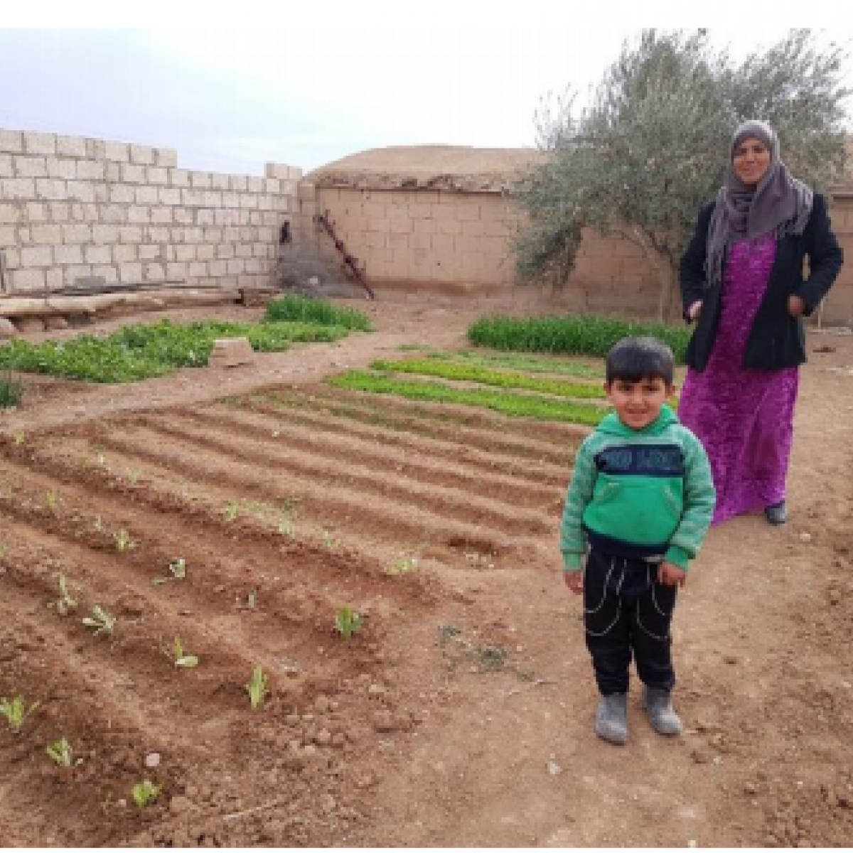 A woman and her young son stand alongside a small home vegetable garden.