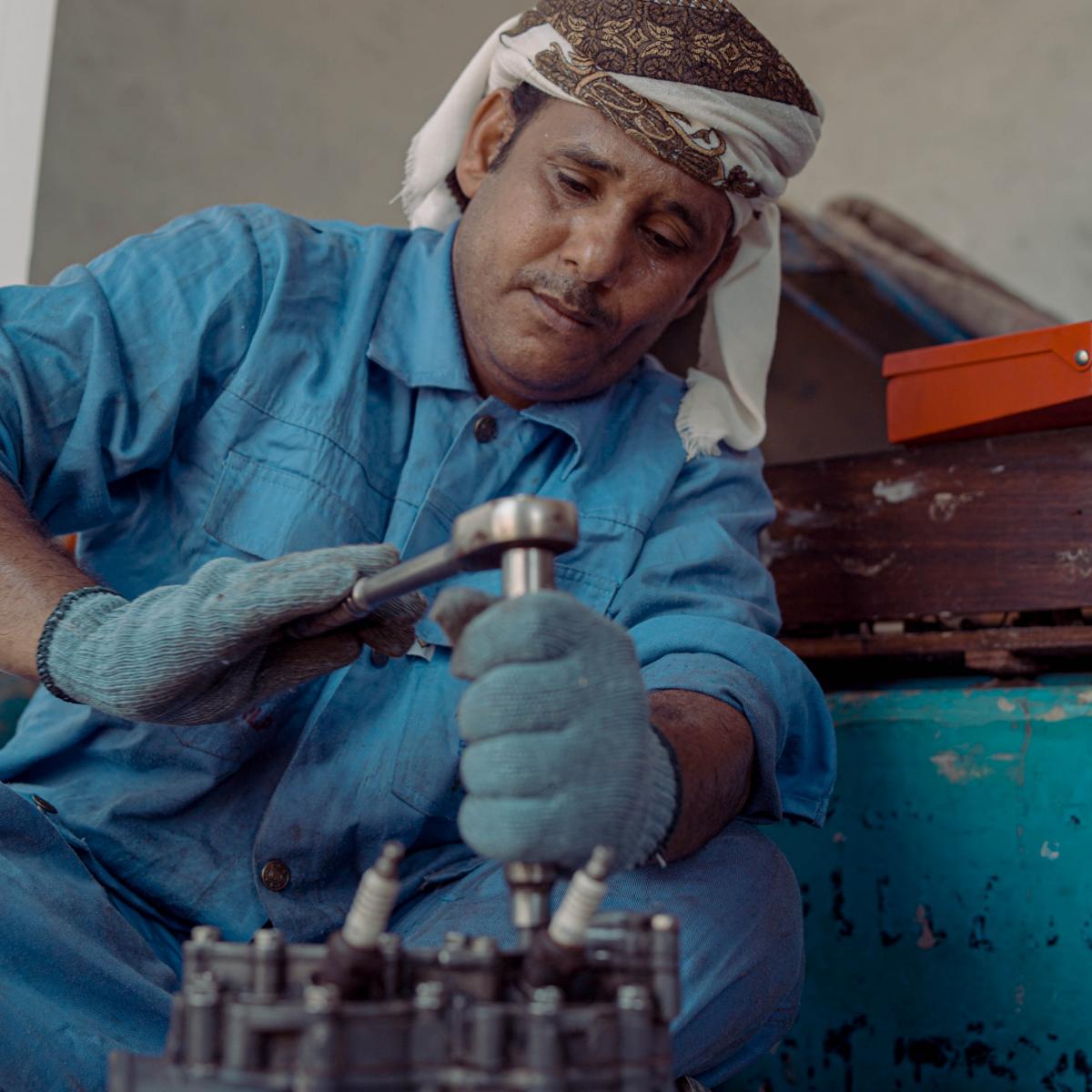 Man seated repairing an engine with tools.
