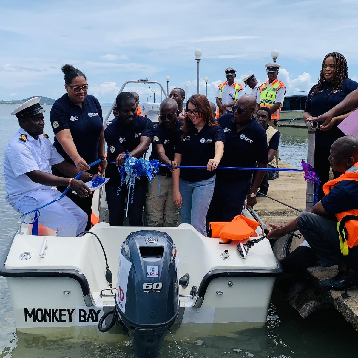USAID and Government of Malawi officials cutting a ribbon in a boat in the presence of other district fisheries officials, law enforcers, and the media.