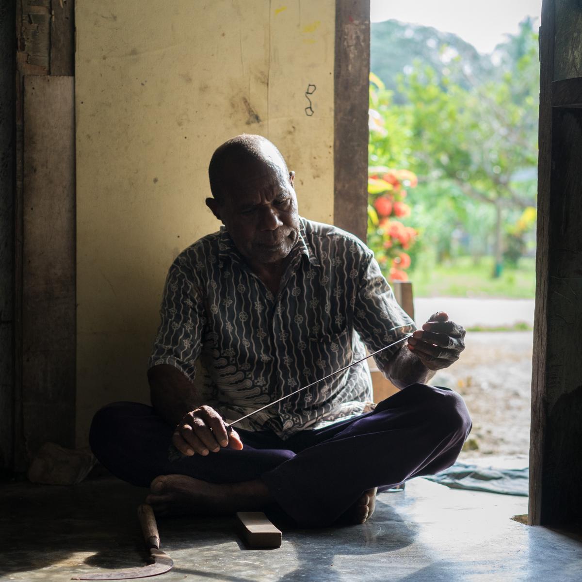 Vanilla farmer Agustinos Daka, 61, sharpens his machete in the courtyard of his house. 