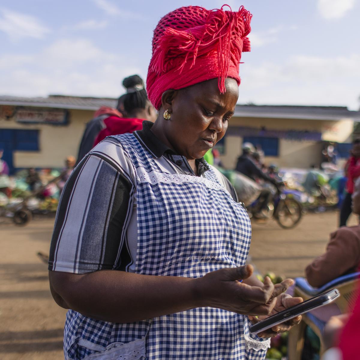 A woman looks down at her smartphone while standing in a busy market.