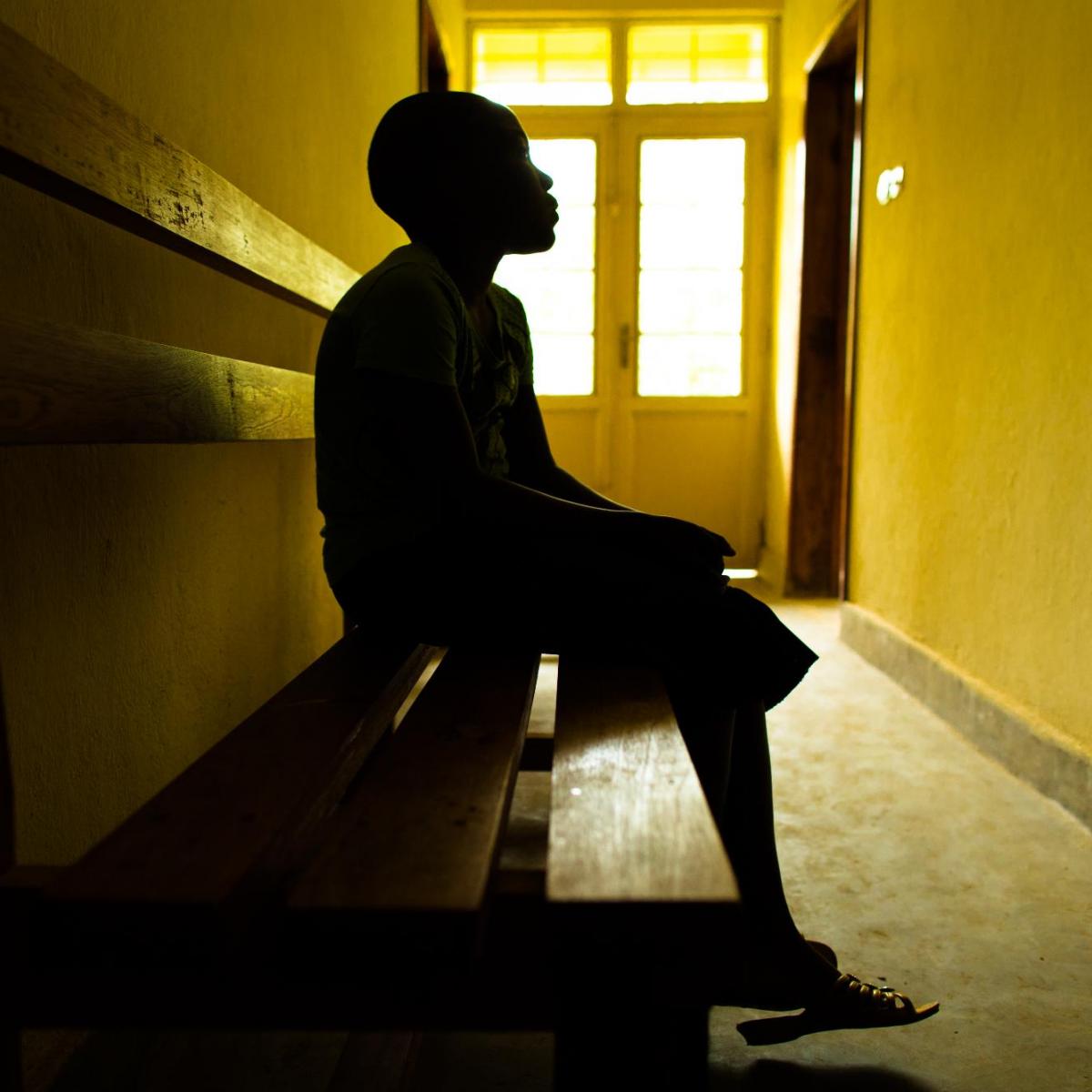 A person in silhouette sits on a bench in a hallway.
