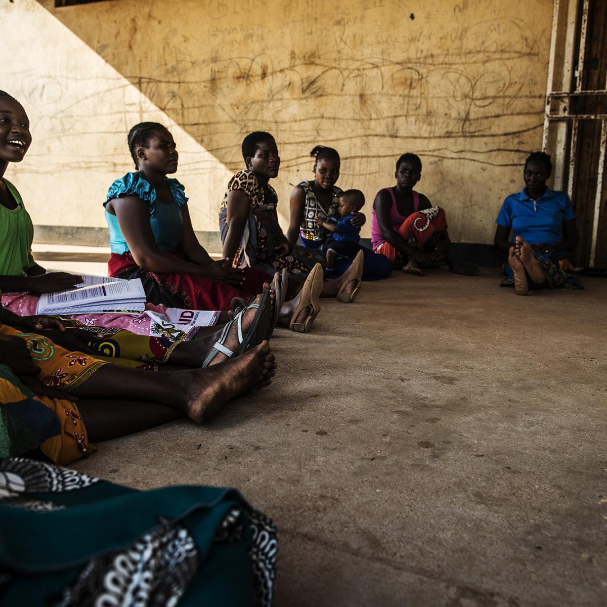 A group of Malawian women sit in a circle in a building courtyard.