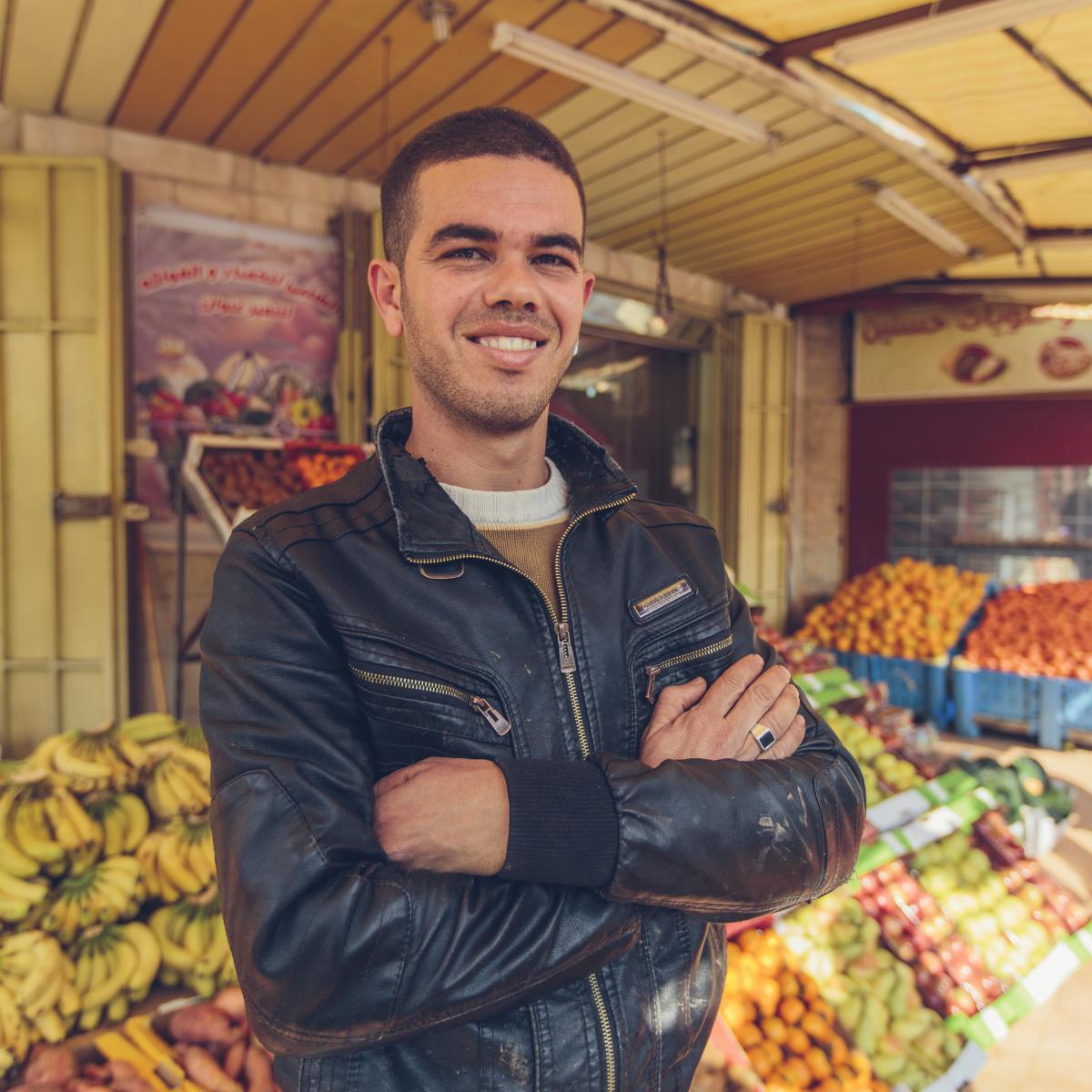 Smiling man with crossed arms in front of a fruit stand.