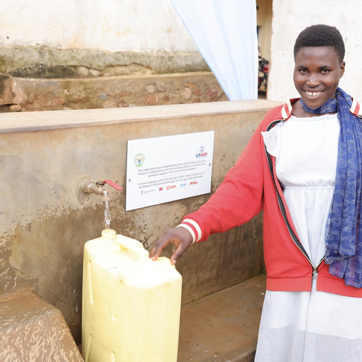 Woman smiling as she fills up her yellow canister full of clean water.