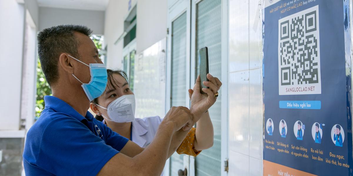 Nurse Le Thi Cam Giang is showing Mr Vu how to scan the QRcode at An Tinh commune health centre so that he can share with his family. 