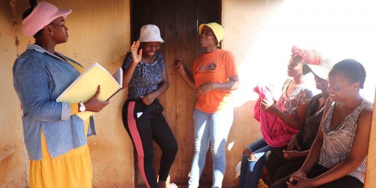 Gcinile (in the white hat) meets with the other young women she runs a chicken egg laying business with and their Business Mentor (carrying a booklet). Gcinile is a champion for HIV prevention in her community. Credit: World Vision