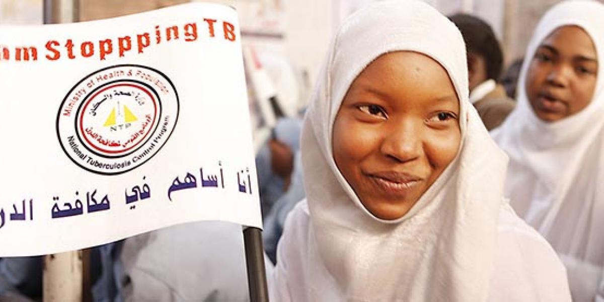 A woman wearing a white head scarf holds up a sign about TB.