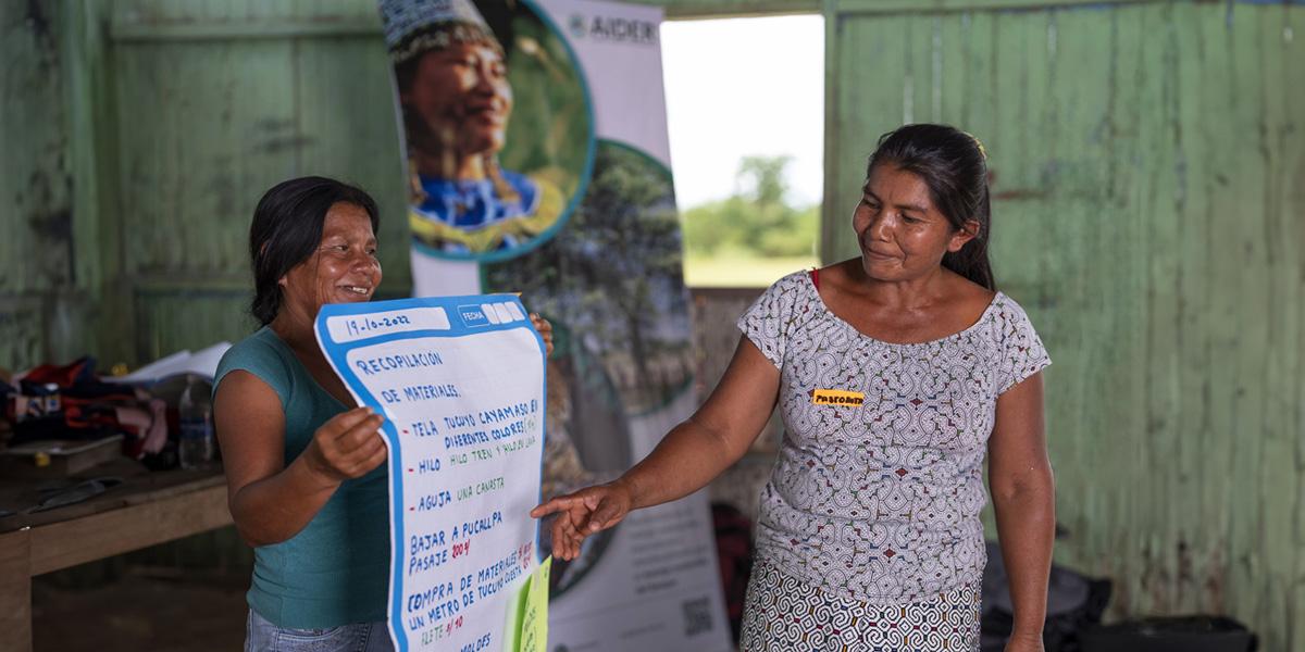 Dos mujeres indígenas sonriendo y realizando una presentación como parte de las actividades de un proyecto