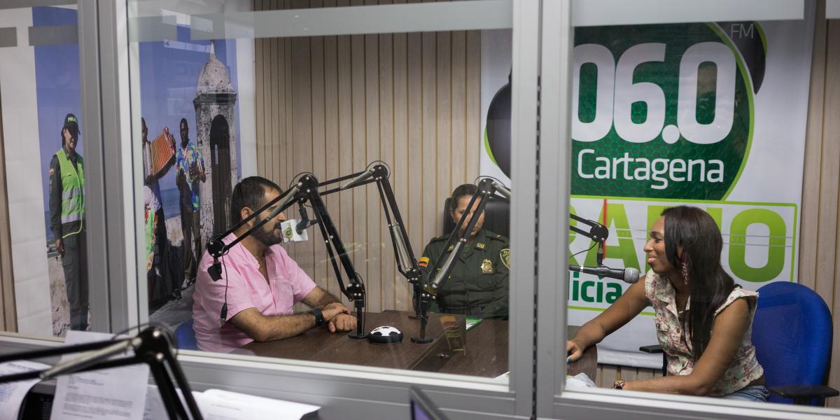Tania, Wilson, and a police officer in a radio station recording booth