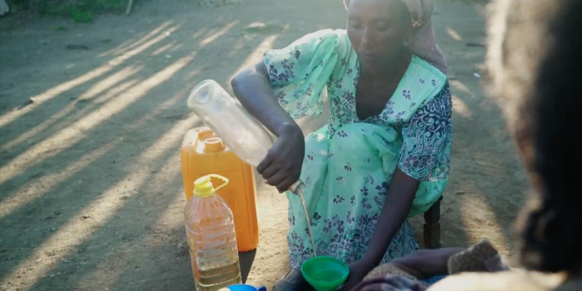 A woman pours oil through a funnel into a bottle.
