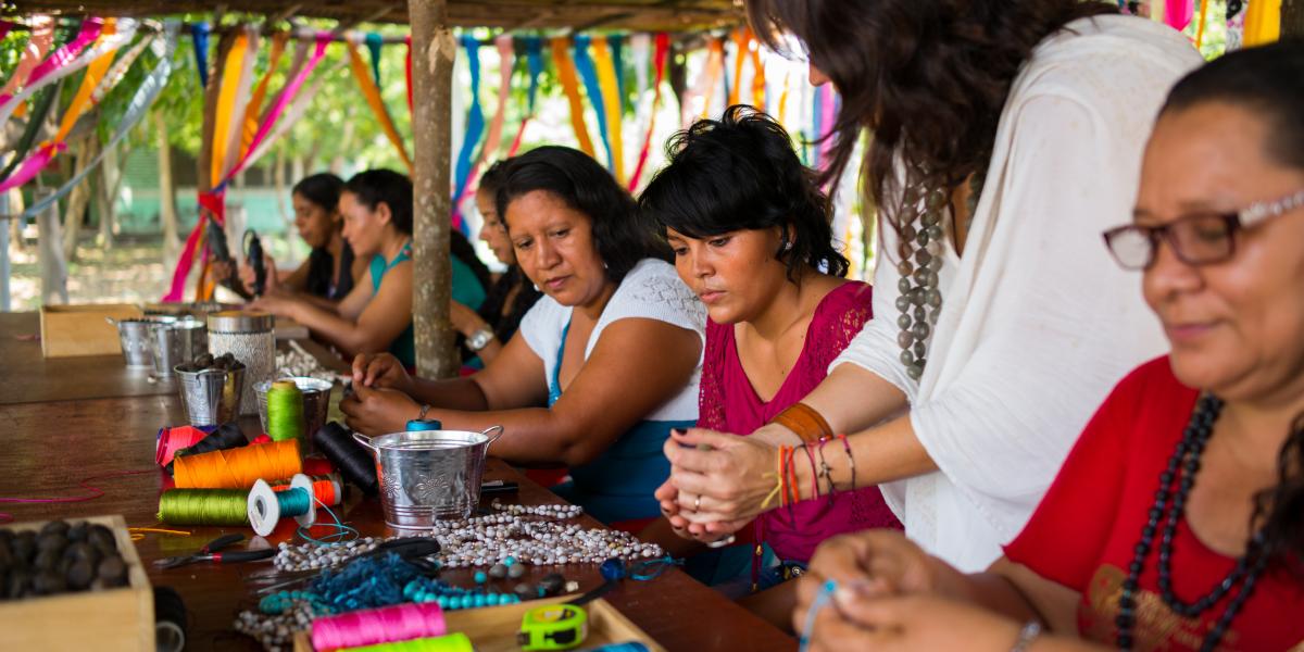 A group of women creating jewelry while sitting at a long table filled with supplies.