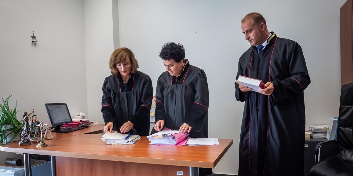 Two women and a man in judges robes look at papers on a desk