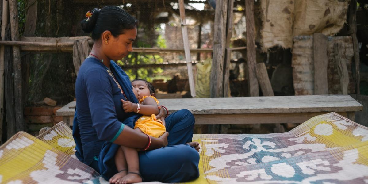 A woman sits on a blanket, breast feeding a young child