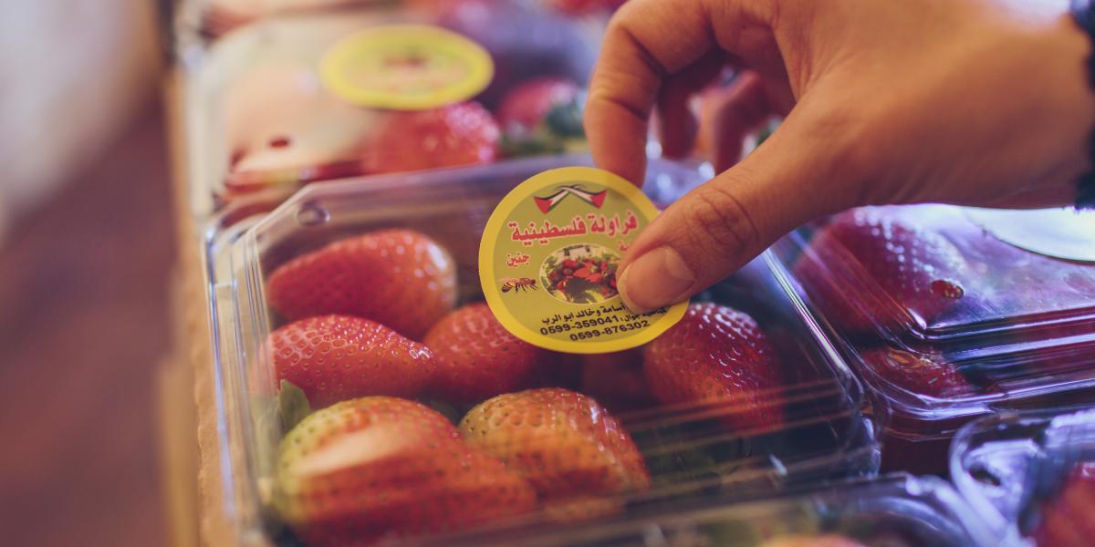 A hand placing a sticker on a box of strawberries.