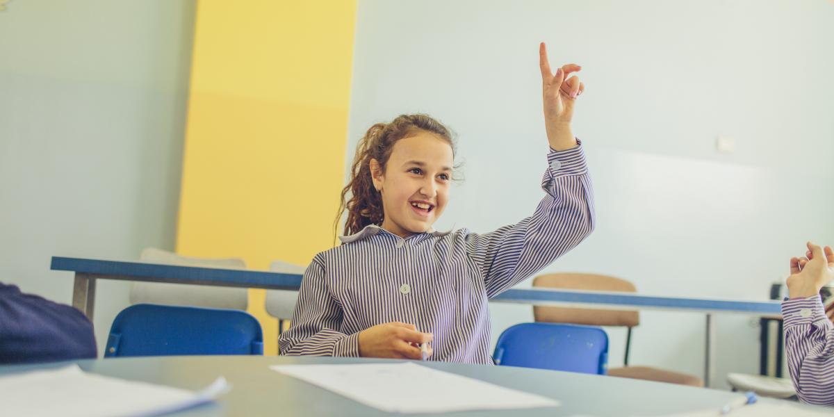A girl raising her hand in her classroom.