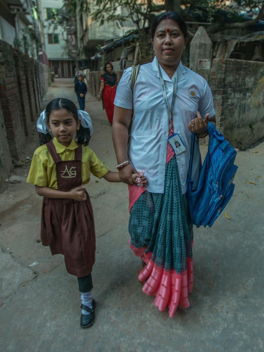 A woman and young girl hold hands as they walk through a neighborhood.