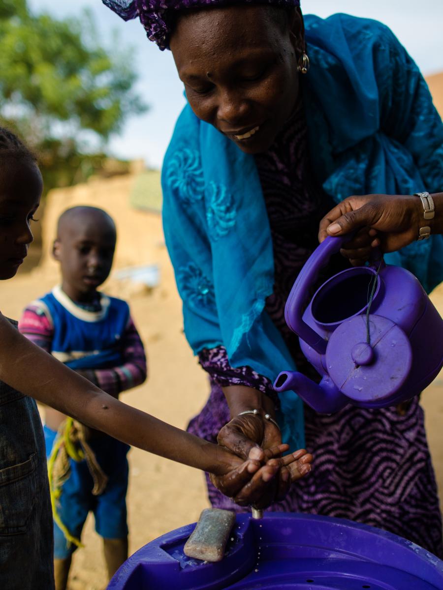 A woman pours water from a blue pitcher onto the hands of a child.