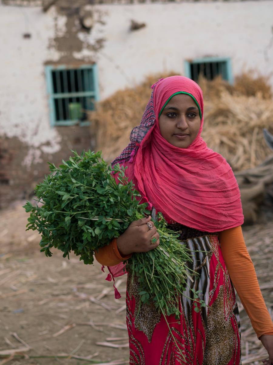 Young woman carrying a bunch of vegetation on her right arm.