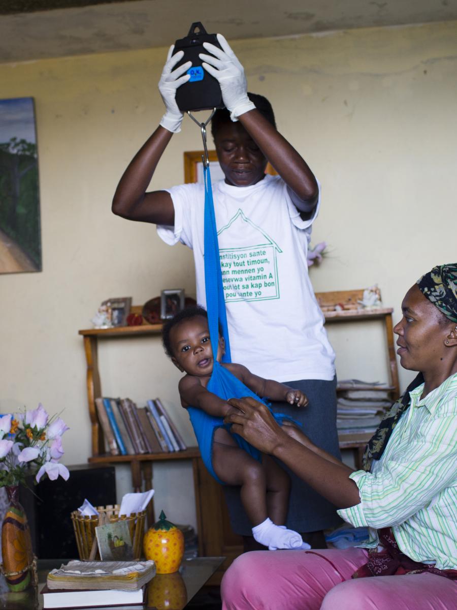 A baby being weighed during a home wellness visit.