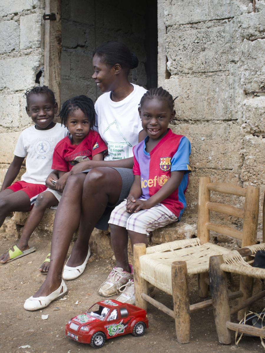 A woman and her young children sit on the stoop outside of their home.