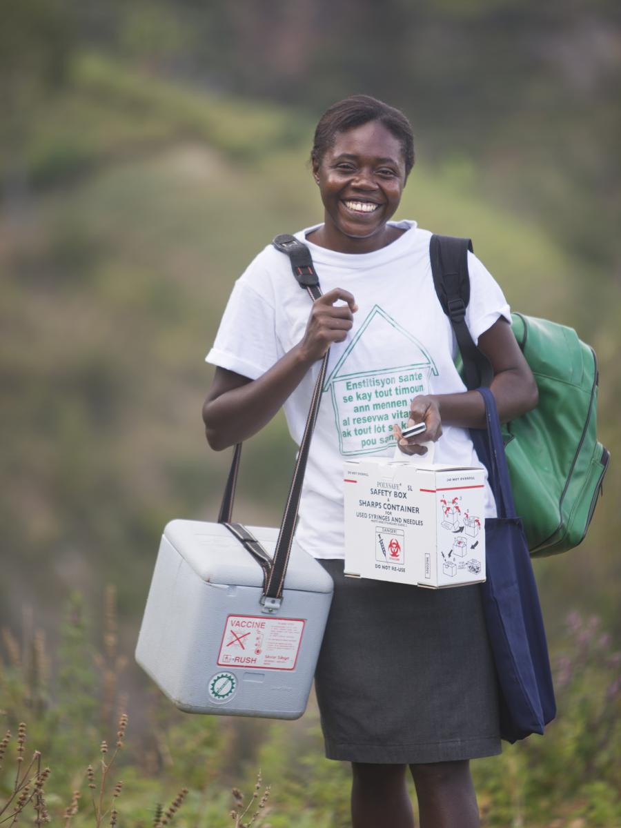 A woman carries supplies in two boxes and a green backpack.