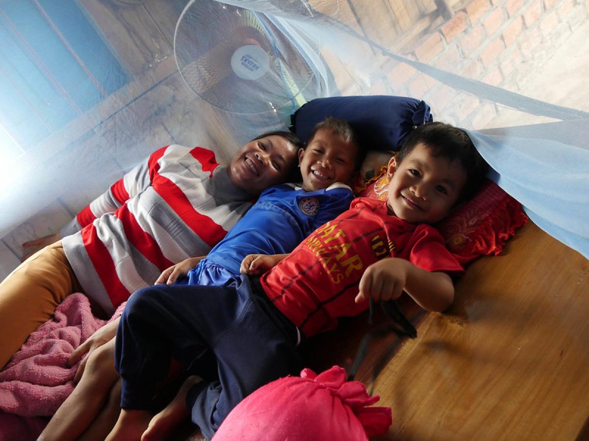 A woman and two boys lie next to each other surrounding by an insecticide-treated net supported by USAID.