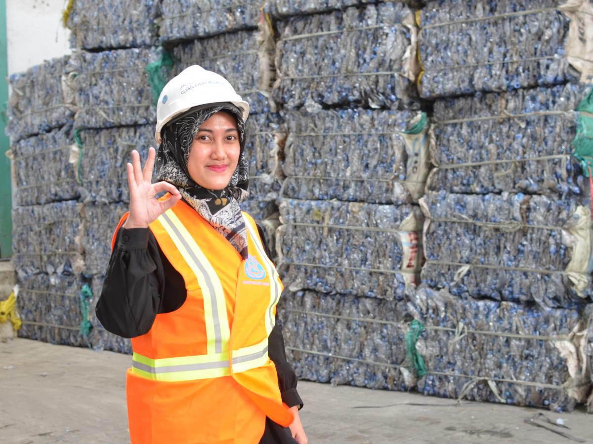 A woman is standing in front of collected plastic waste. 