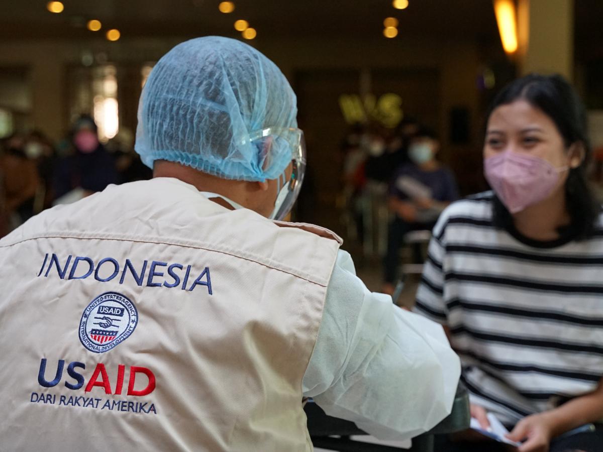 Health worker in Indonesia wearing personal protective equipment shares information with a patient after she received a COVID-19 vaccine.