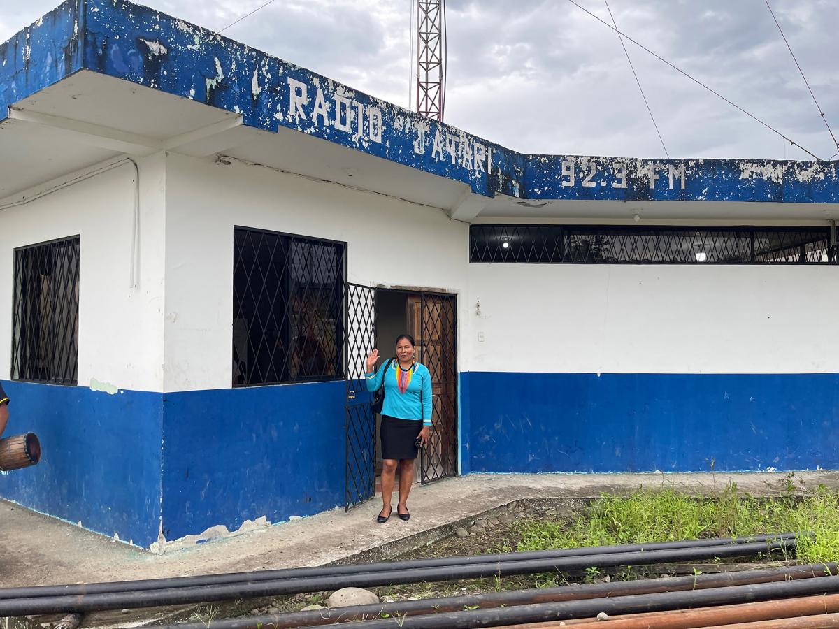 Una mujer indígena Kichwa de pie y saludando en la entrada de la estación de radio.