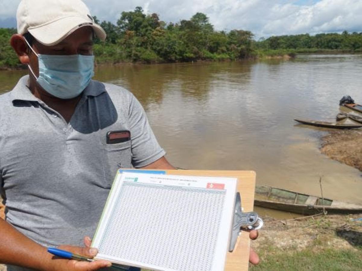 A man showing a table filled with data from trees in front of an amazonian river